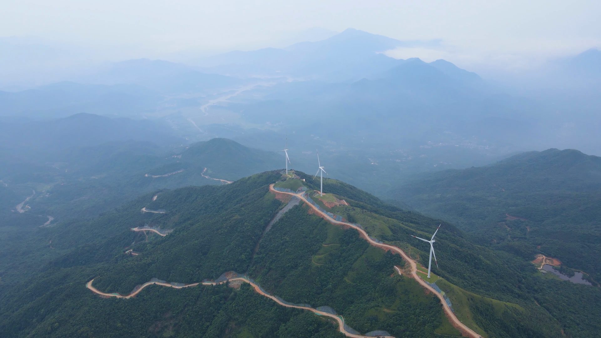 Wind farm on green hills with turbines in light haze